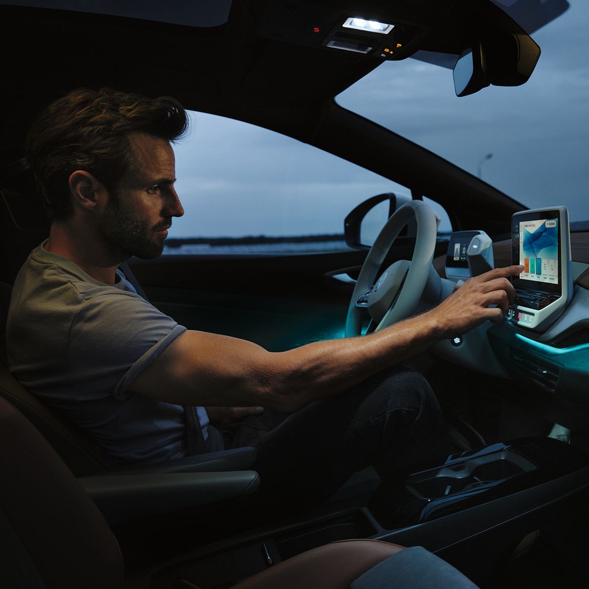 Mann sitzt auf der Fahrerseite des VW ID.4 und bedient den Touchscreen