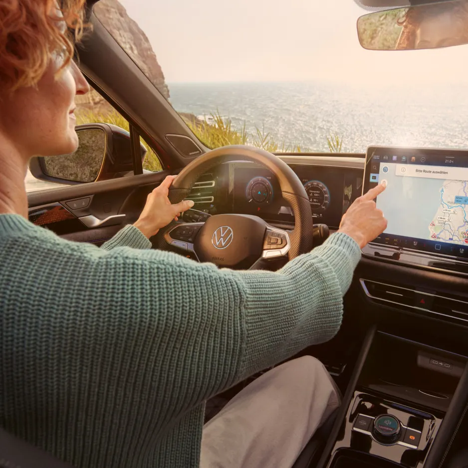 Frau sitzt auf dem Fahrersitz eines geparkten VW Tiguan und bedient den Touchscreen des Infotainment-Systems mit Kartenansicht.