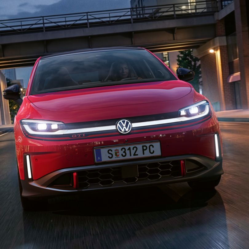 Eine Person fährt einen roten VW ID. Polo GTI durch ein modern beleuchtetes Geschäftsviertel am Abend.