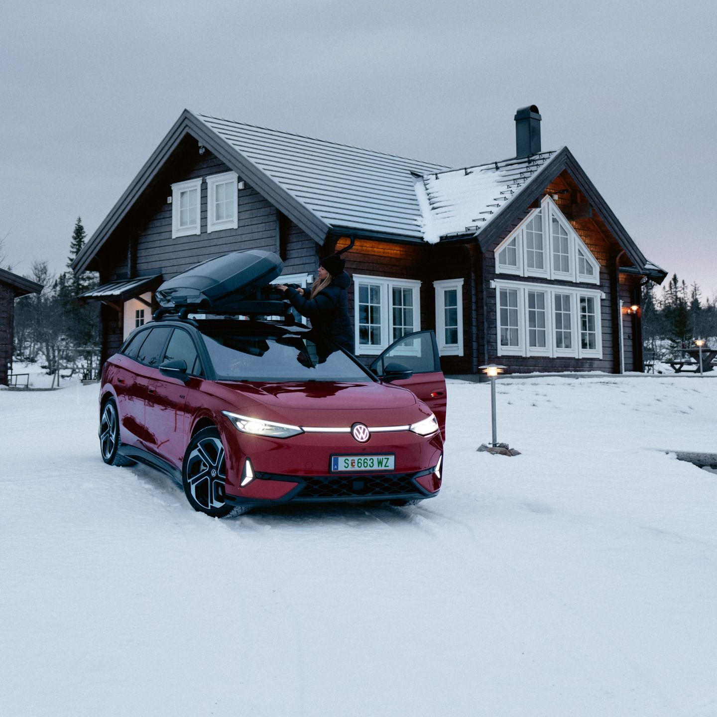 Ein roter ID.7 Tourer GTX mit Dachbox steht im Schnee vor einem Wohnhaus. 