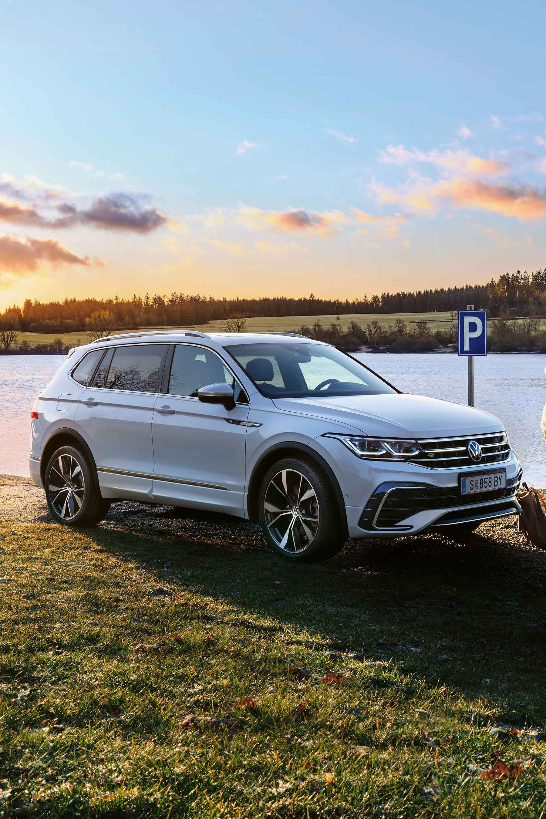 Mann steht neben einem weißen VW Tiguan Allspace, der am Seeufer geparkt ist