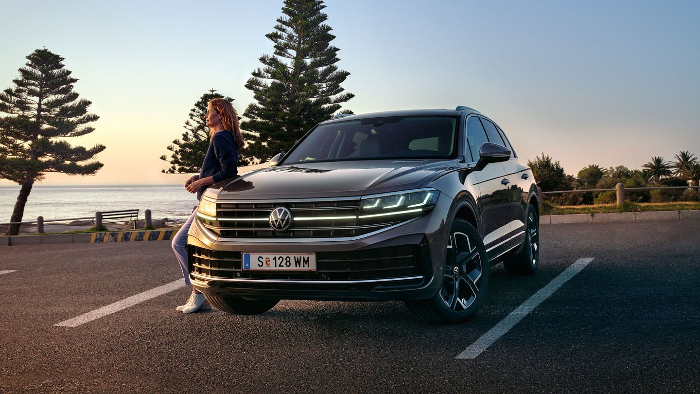 Ein VW Touareg Elegance in der Dämmerung am Meer mit eingeschalteten HD-Matrix-Scheinwerfern. 