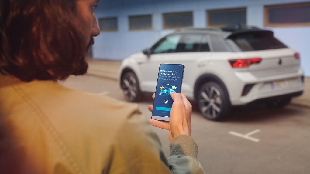 VW T-Roc R-Line in weiß vor einem Gebäude, Seite sichtbar, Mann steht mit Smartphone im Vordergrund