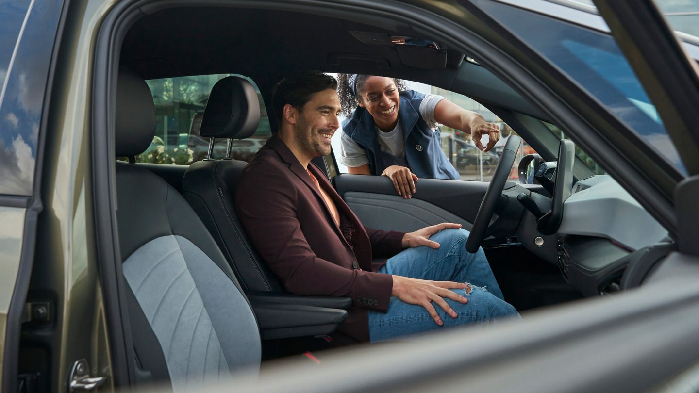 Eine Servicemitarbeiterin zeigt einem Mann im VW ID.5 eine Funktion im Infotainmentsystem.