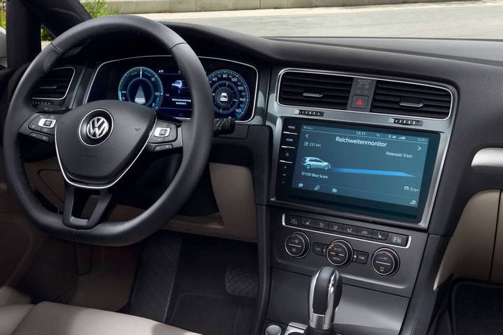 Das Bild zeigt das Innere eines VW e-Golf, besonders das Armaturenbrett. Es sind das Lenkrad, die Instrumententafel und ein großer Touchscreen-Bildschirm sichtbar.