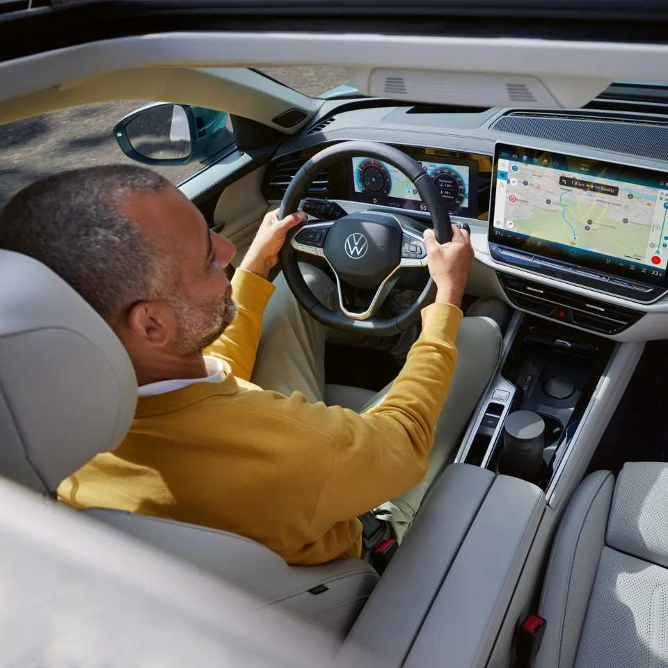 Blick von oben durch das geöffnete optionale Schiebedach des VW Passat, in dem ein Mann am Steuer sitzt.