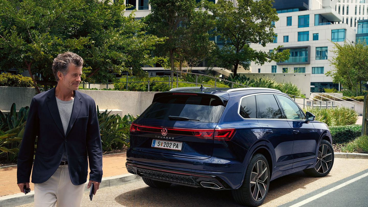 Ein Mann überquert die Straße, schräg hinter ihm ein am Straßenrand parkender VW Touareg R-Line.