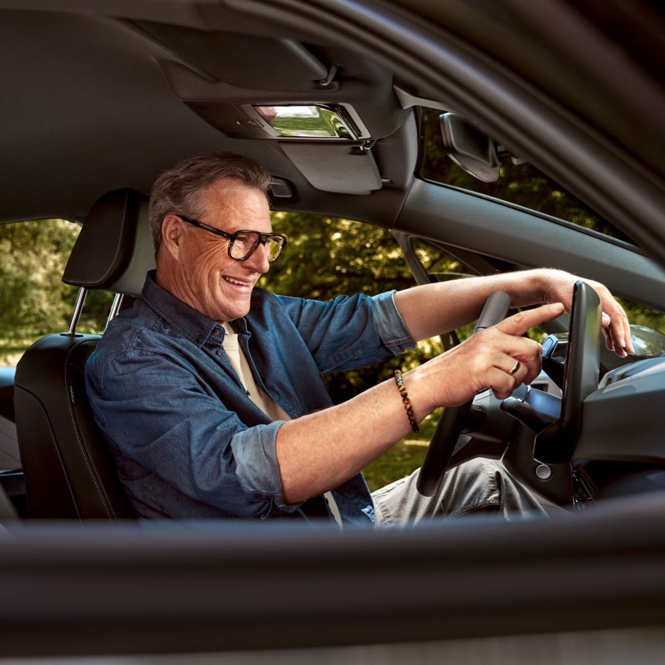 Ein Mann sitzt auf dem Fahrersitz seines geparkten ID.3 und tippt auf das HMI