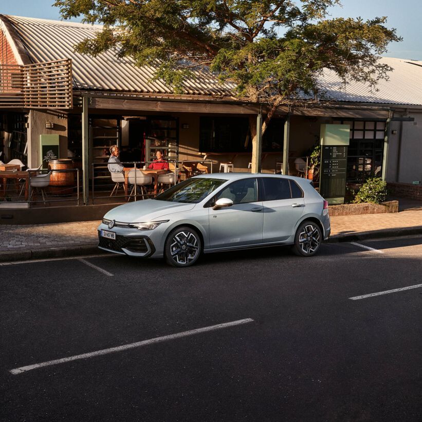 Seitenansicht eines grauen VW Golf, der vor einem Lokal parkt.