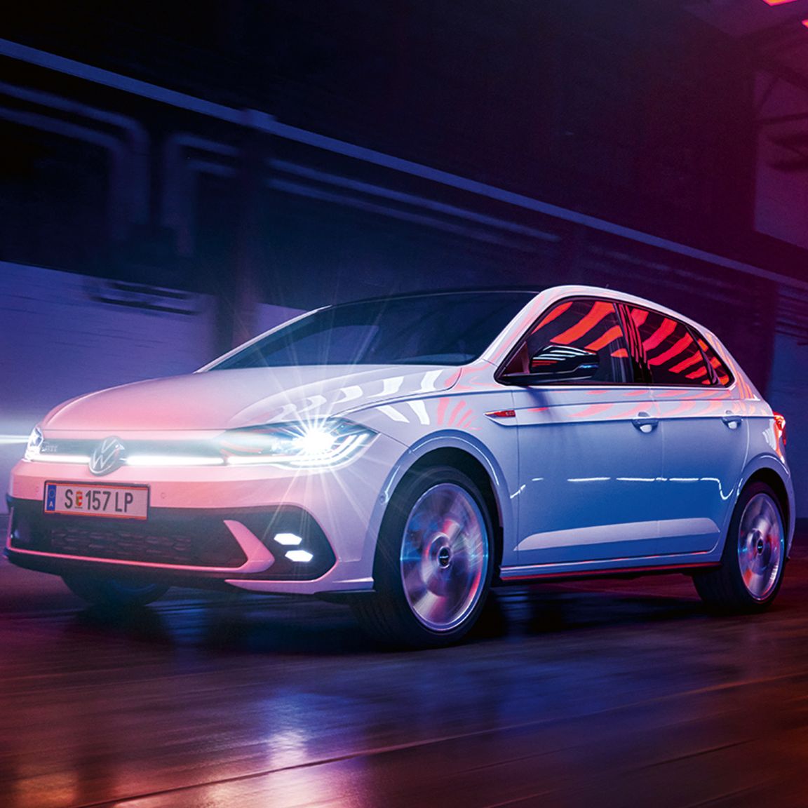 Ein weißer VW Polo GTI mit aktiven Scheinwerfern fährt in einer dunklen Halle.