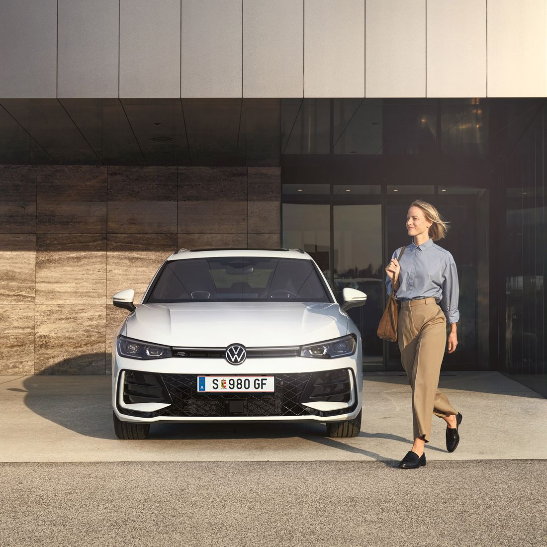 Frontansicht eines weißen VW Passat R-Line, eine Frau geht an ihm vorbei.