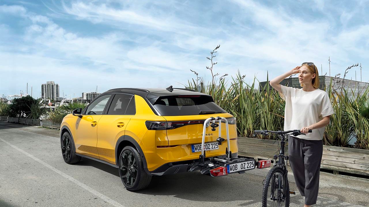 Eine Person mit einem Fahrrad steht neben einem gelben Volkswagen T-Roc mit Fahrradheckträger.