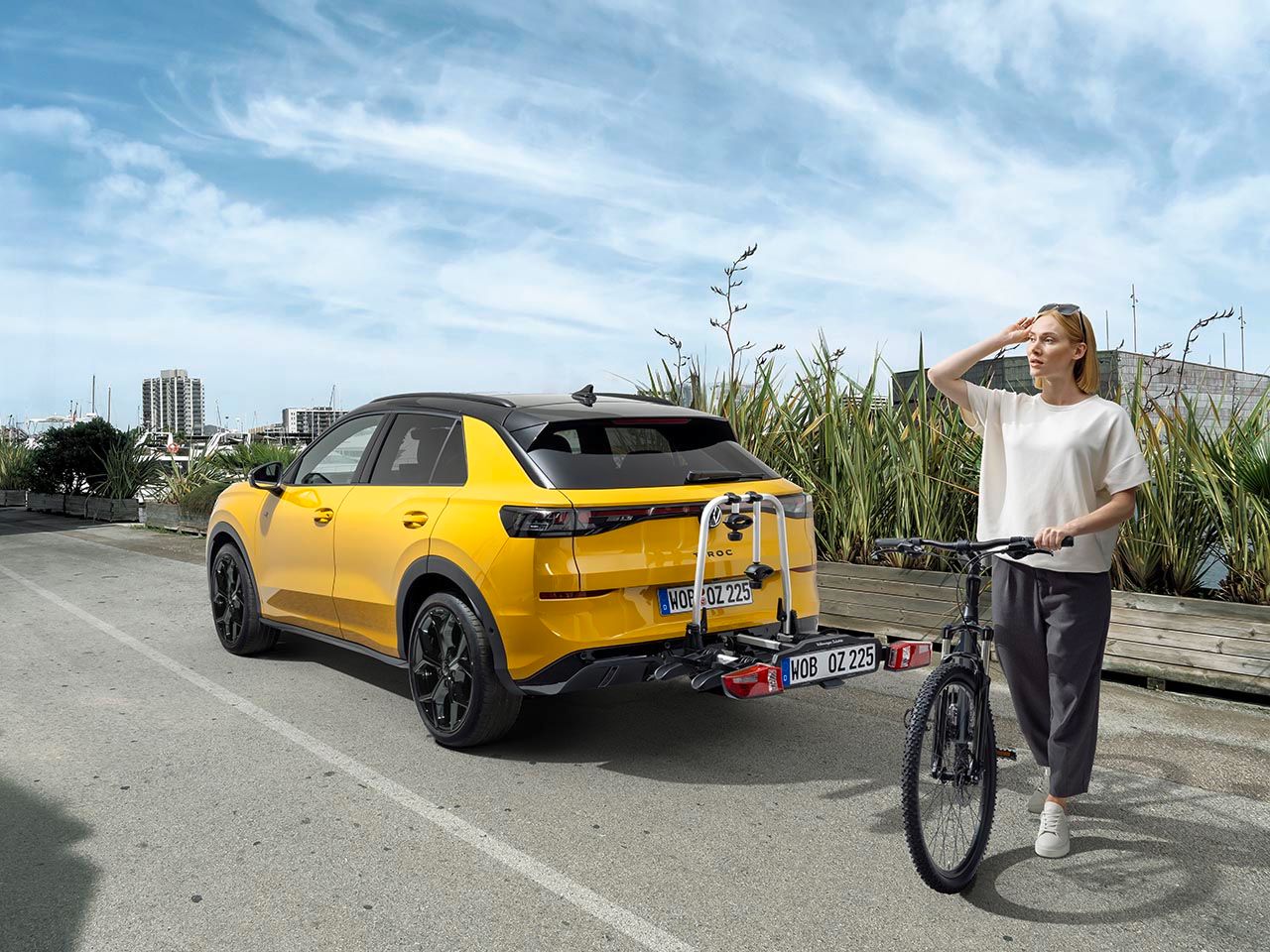 Eine Person mit einem Fahrrad steht neben einem gelben Volkswagen T-Roc mit Fahrradheckträger.