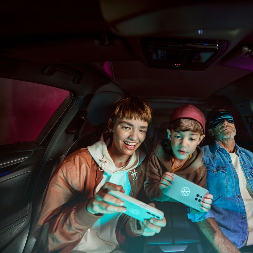 Vater mit zwei Kindern im Volkswagen, die Kinder spielen mit der AirConsole.