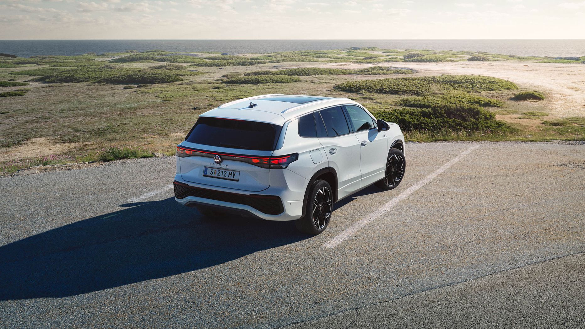 Heckansicht eines weißen VW Tayron auf einem Parkplatz in Dünen.