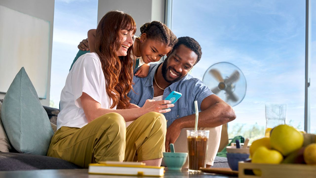 Eine Familie sitzt auf dem Sofa und schaut glücklich in ein Smartphone.