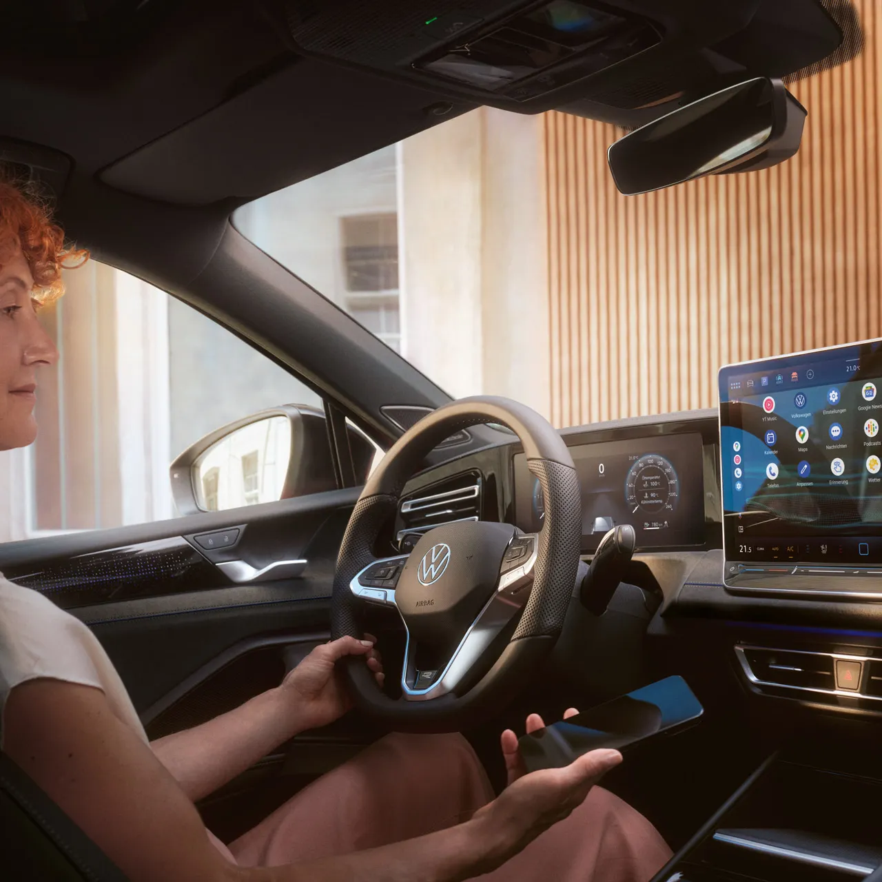 Eine Frau auf dem Fahrersitz des Tiguan hält ein Smartphone in der Hand und blickt auf den Bildschirm des Infotainment-Systems.