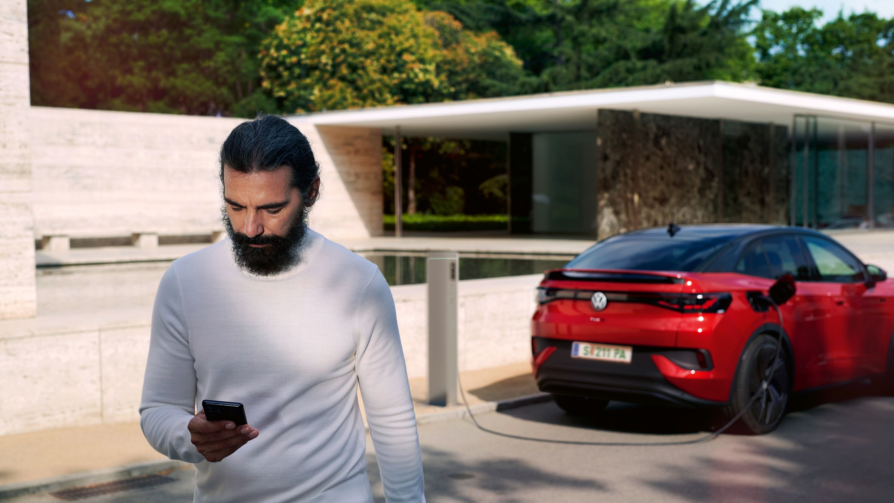 Mann liest ID. Newsletter von Volkswagen Österreich, sein roter VW ID.5 GTX wird geladen
