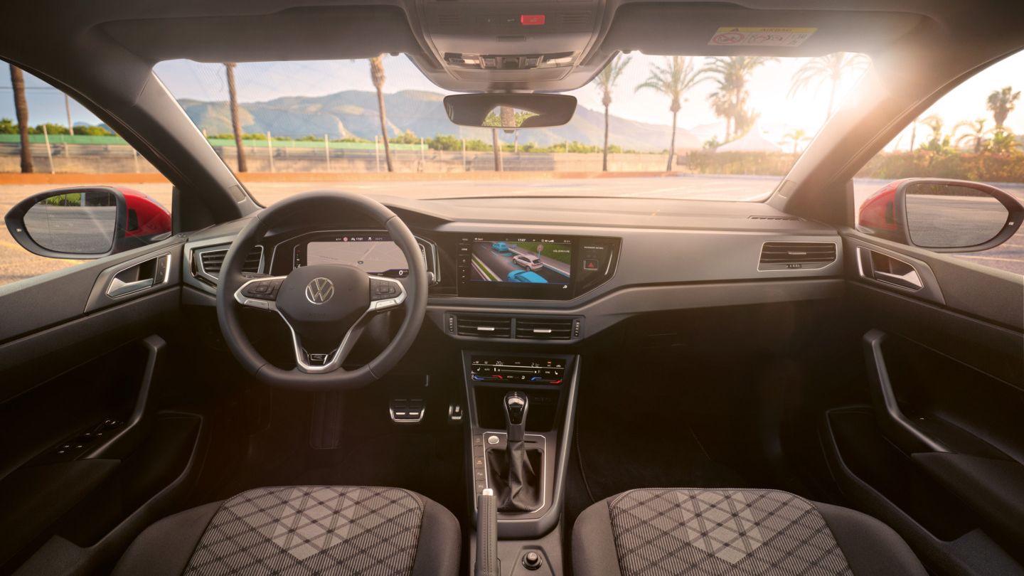 Blick auf das Cockpit mit Lenkrad und Infotainment-System im VW Taigo. Vor dem Fahrzeug sind Palmen und Berge.