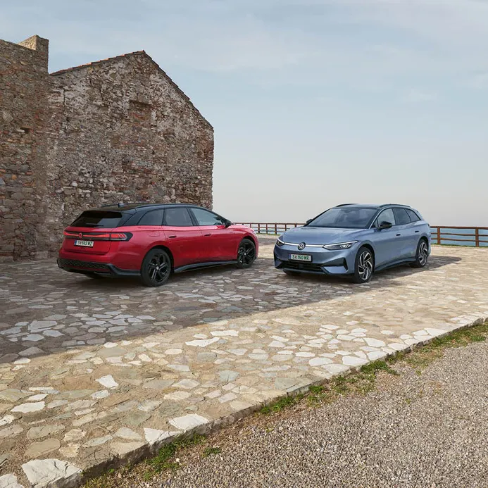 Ein roter VW ID.7 GTX Tourer und ein blauer VW ID.7 Tourer stehen auf einer Parkfläche am Meer.