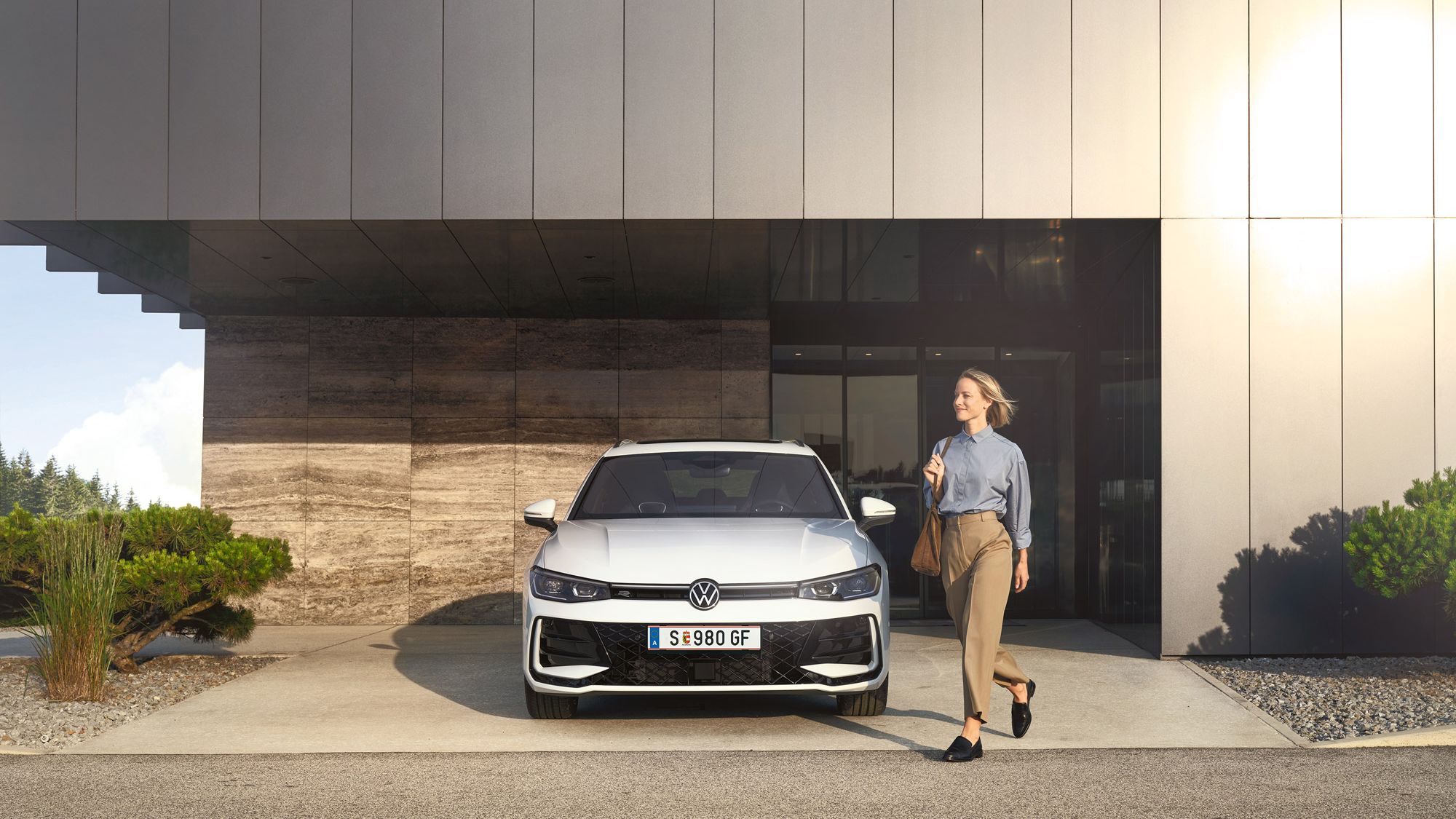 Frontansicht eines weißen VW Passat R-Line, eine Frau geht an ihm vorbei.