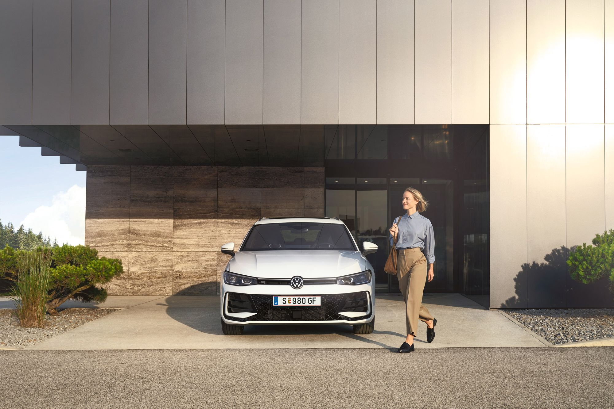 Frontansicht eines weißen VW Passat R-Line, eine Frau geht an ihm vorbei.