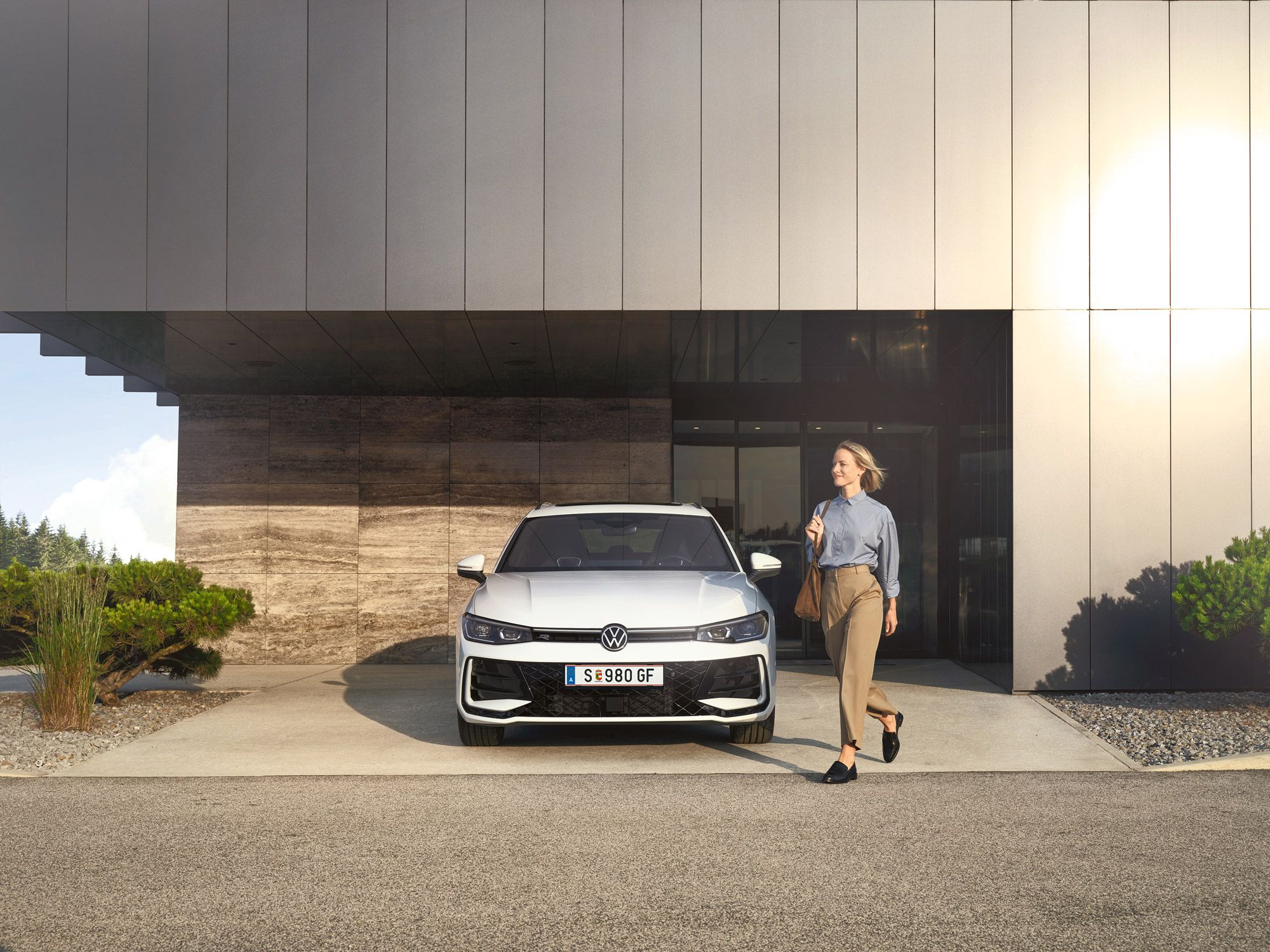 Frontansicht eines weißen VW Passat R-Line, eine Frau geht an ihm vorbei.