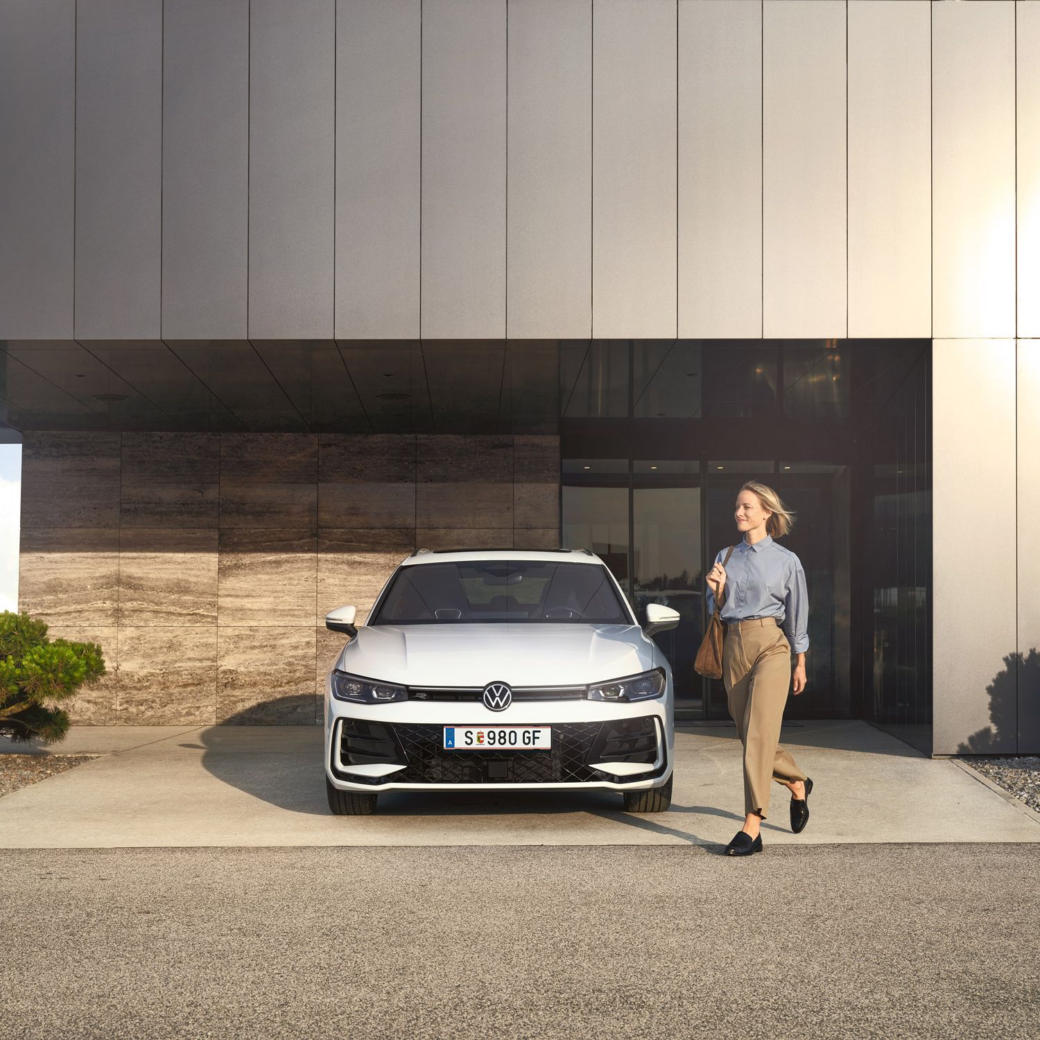 Frontansicht eines weißen VW Passat R-Line, eine Frau geht an ihm vorbei.