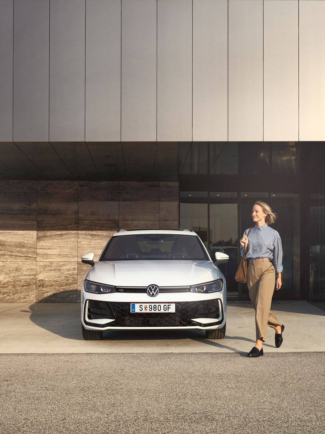 Frontansicht eines weißen VW Passat R-Line, eine Frau geht an ihm vorbei.