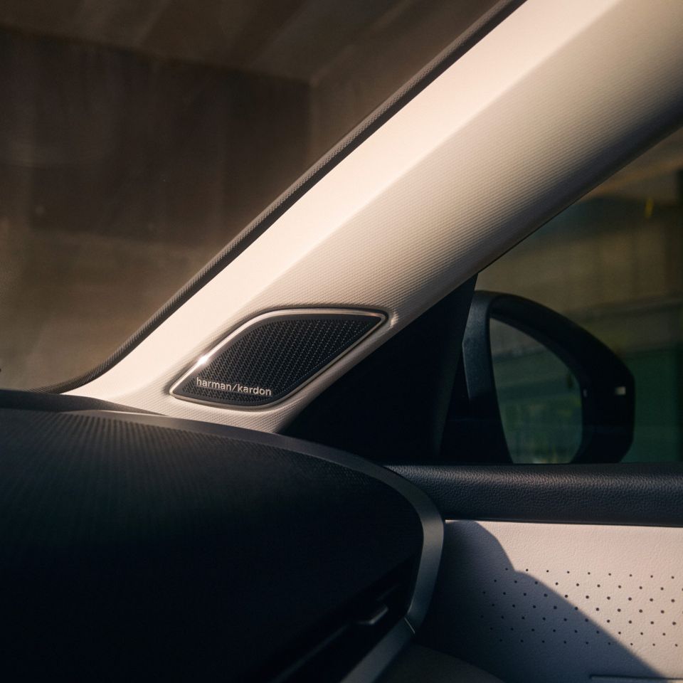 Nahaufnahme des Innenraums eines T-Roc, mit Fokus auf dem Lautsprecher von Harman Kardon in der A-Säule. Man sieht auch einen Teil des Schiebedachs und der Seitenspiegel des Fahrzeugs.