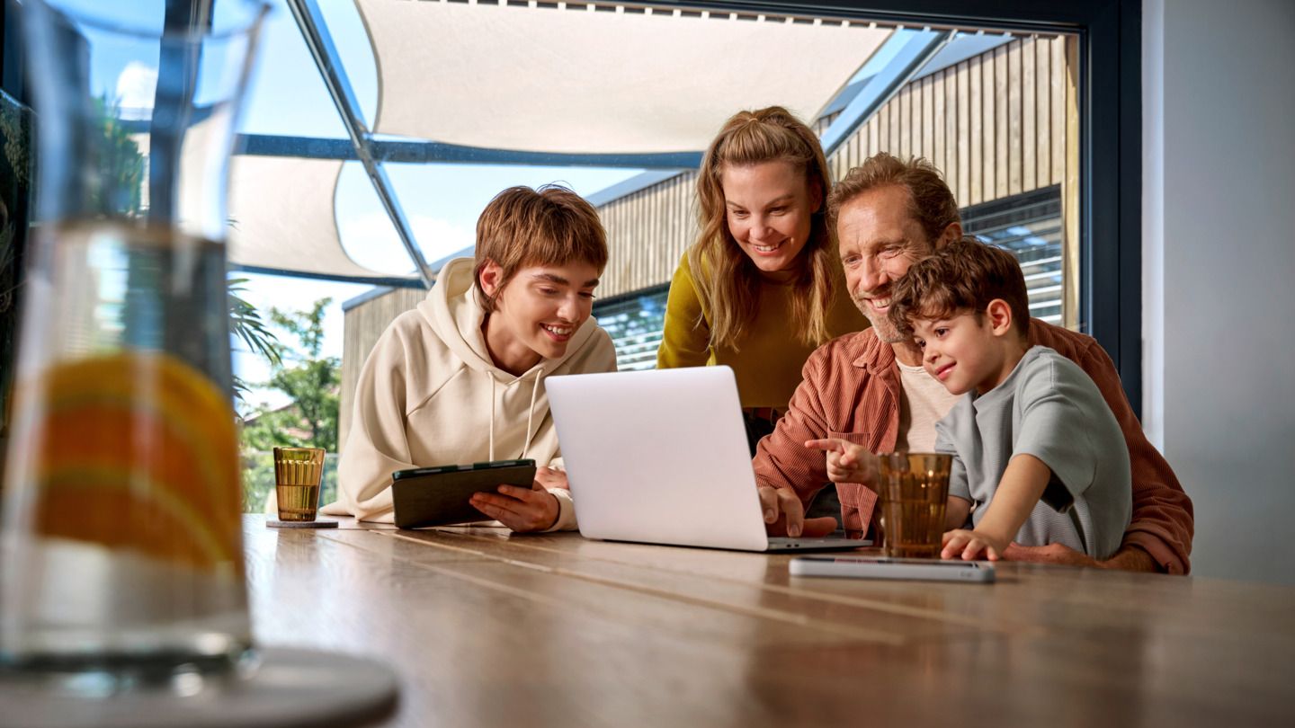 Eine Familie sitzt zusammen am Tisch und schauen glücklich auf einen Laptop. 