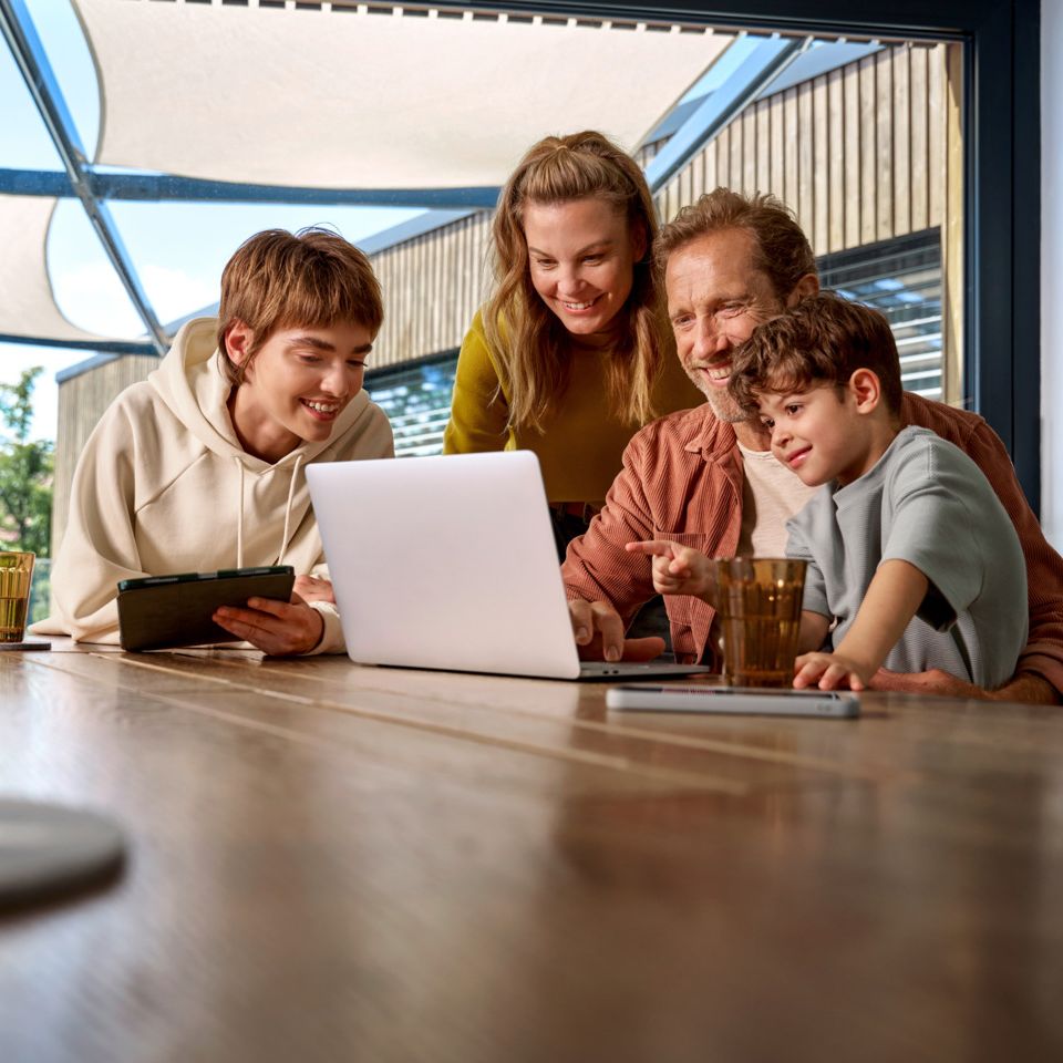 Eine Familie sitzt zusammen am Tisch und schauen glücklich auf einen Laptop. 