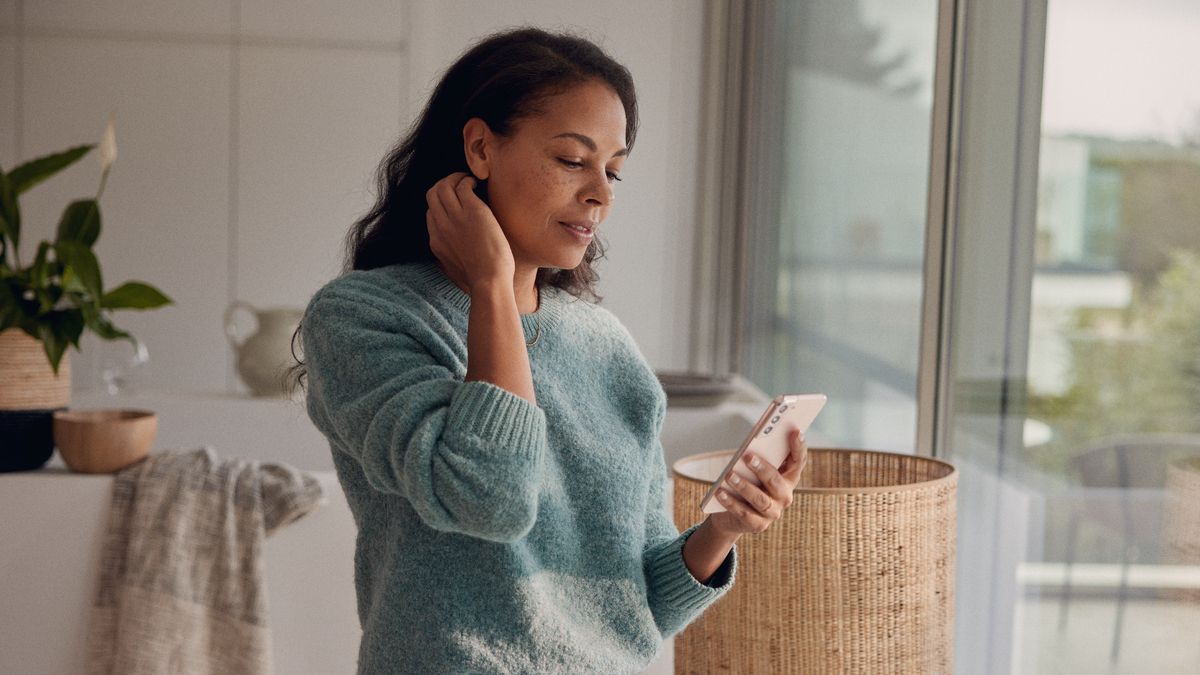 Eine Frau steht am Fenster und blickt auf ihr Smartphone