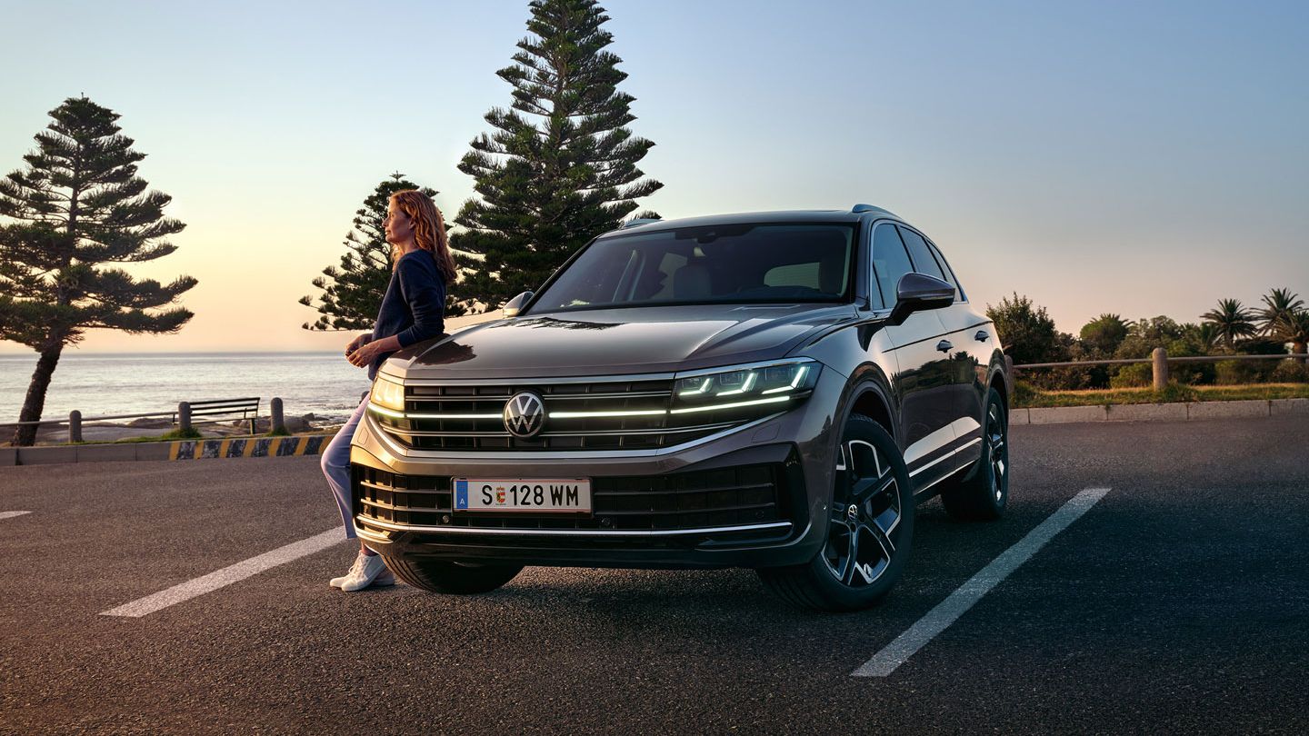Ein VW Touareg Elegance in der Dämmerung am Meer mit eingeschalteten HD-Matrix-Scheinwerfern. 