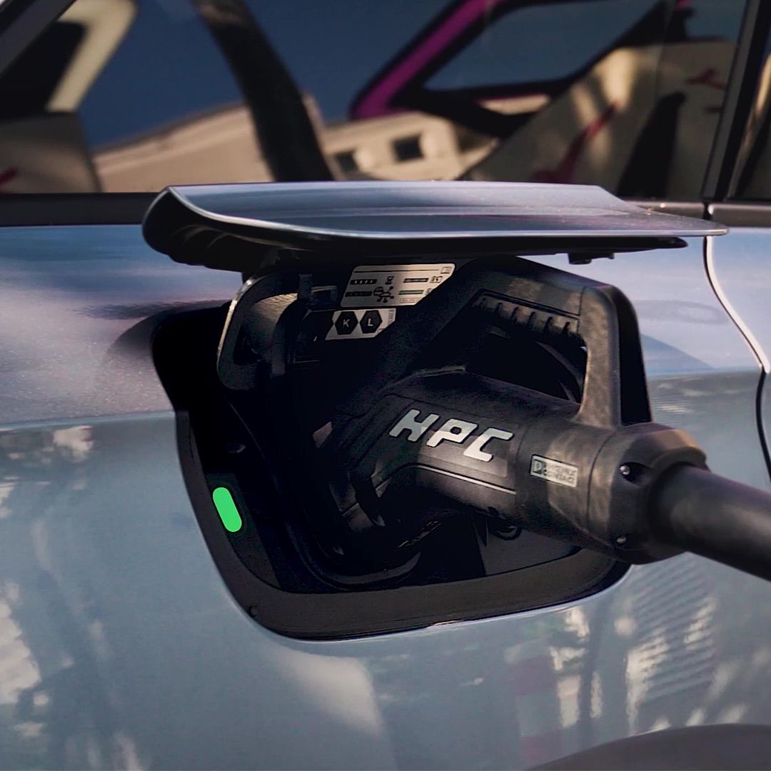 Ein elektrisches Fahrzeug wird mit einem Schnellladegerät geladen. Das Kabel ist in den Ladeanschluss des Autos eingesteckt. Der Ladeanschluss ist geöffnet und zeigt den Ladevorgang.
