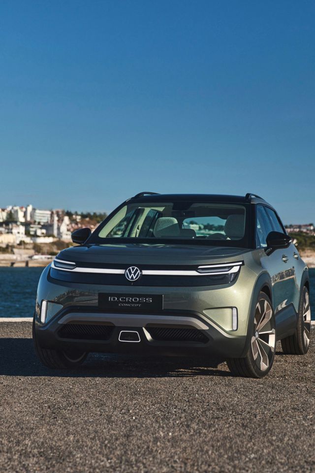 Ein grüner Volkswagen ID. Cross steht vor einem Wasserhintergrund mit Stadtansicht. Das Auto ist von vorne gesehen und strahlt in der Sonne. Es gibt keine anderen Fahrzeuge oder Personen im Bild.