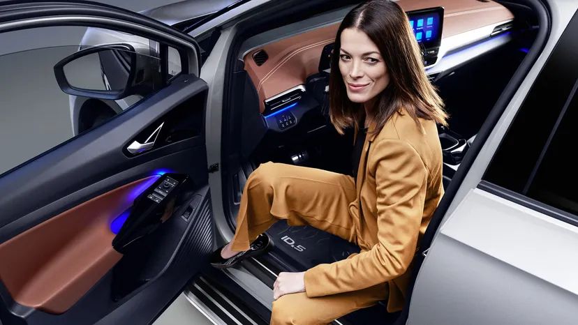 Eine Frau im senfgelben Hosenanzug steigt aus einem Volkswagen ID.5 aus und blickt lächelnd in die Kamera.