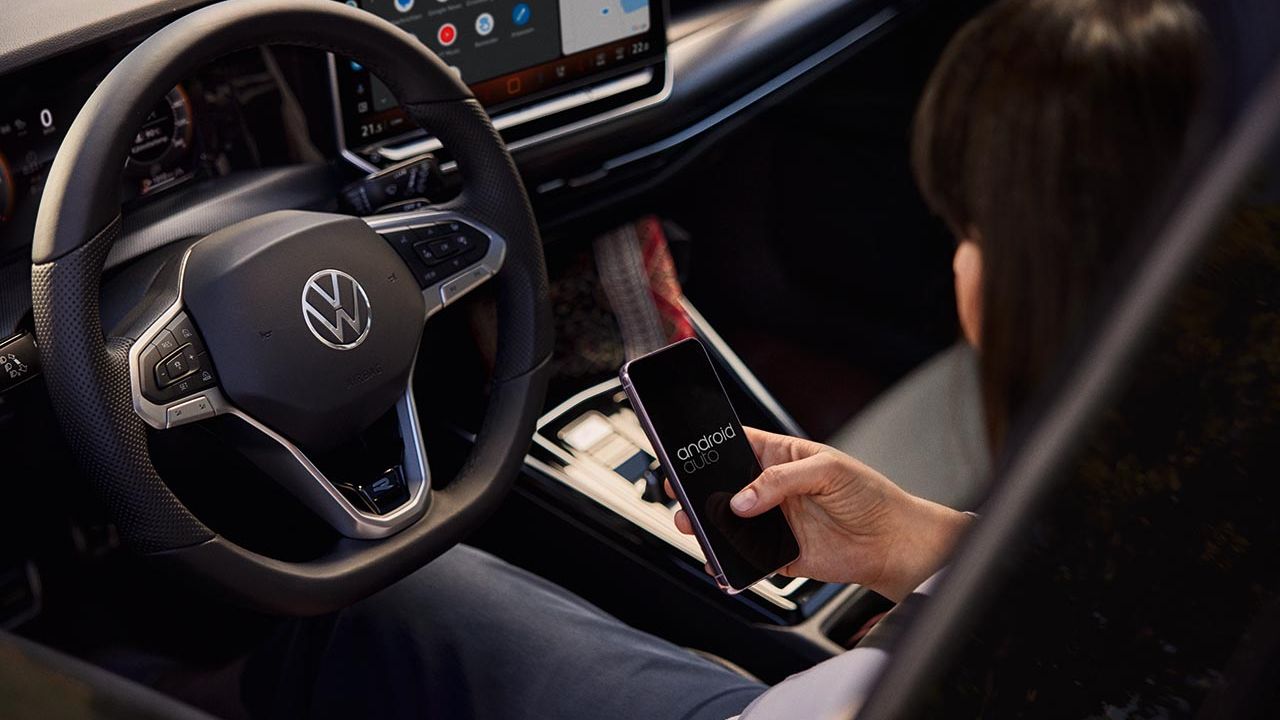 Eine Frau sitzt auf dem Fahrersitz eines VW Golf und bedient ihr Handy.