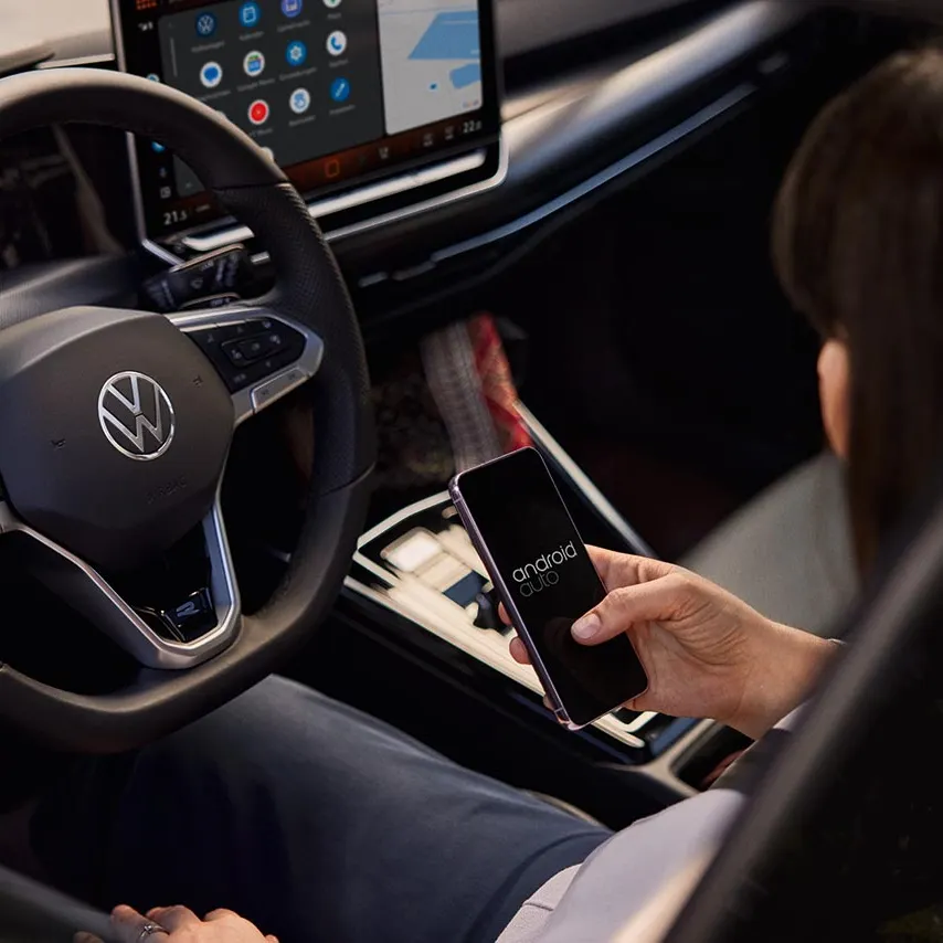 Eine Frau sitzt auf dem Fahrersitz eines VW Golf und bedient ihr Handy.