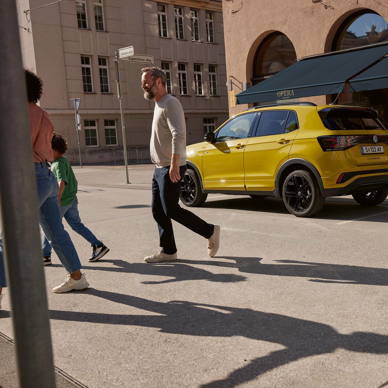 Ein gelber VW T-Cross parkt vor einem Café. Eine Familie geht davor über die Straße.