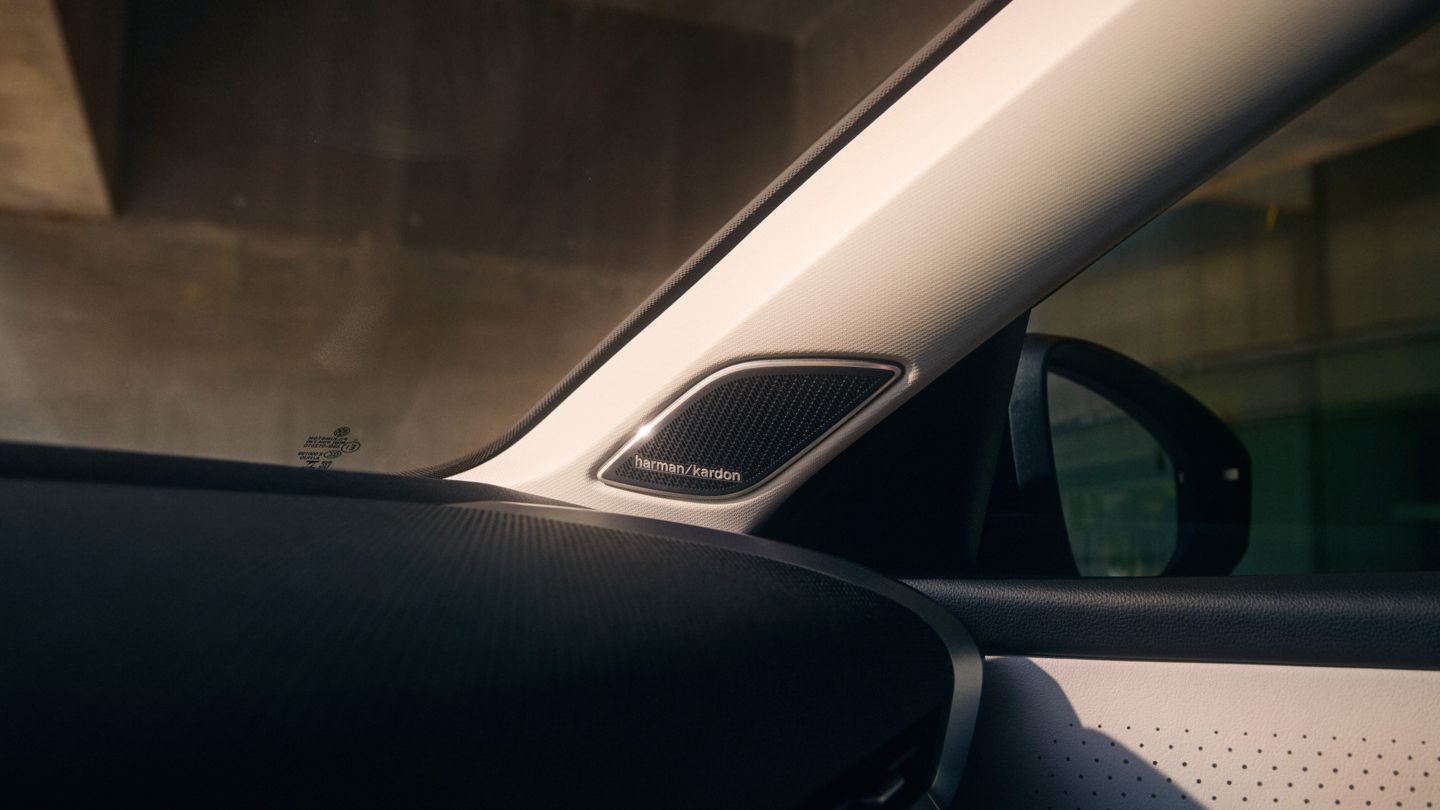 Nahaufnahme des Innenraums eines T-Roc, mit Fokus auf dem Lautsprecher von Harman Kardon in der A-Säule. Man sieht auch einen Teil des Schiebedachs und der Seitenspiegel des Fahrzeugs.
