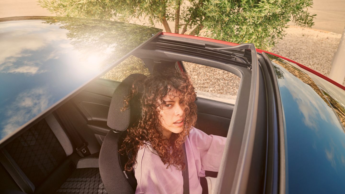 Blick von oben auf VW Taigo mit offenem Panorama-Ausstell-/Schiebedach. Eine Frau schaut von innen heraus.