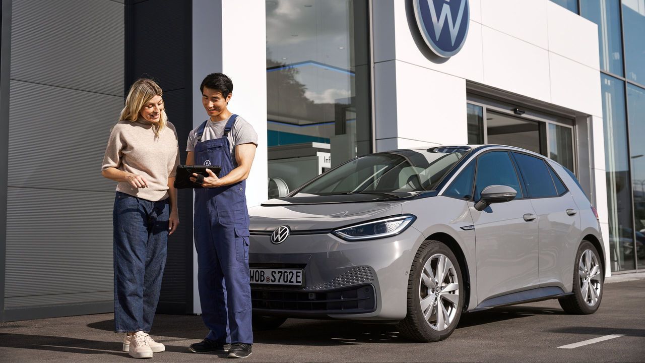 Ein Volkswagen Techniker und eine Kundin stehen vor einem grauen Volkswagen ID.3