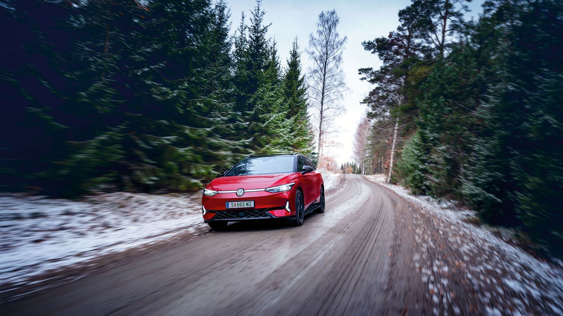 Ein roter VW ID.7 GTX Tourer fährt auf einem Waldweg, auf dem Boden liegt Schnee.