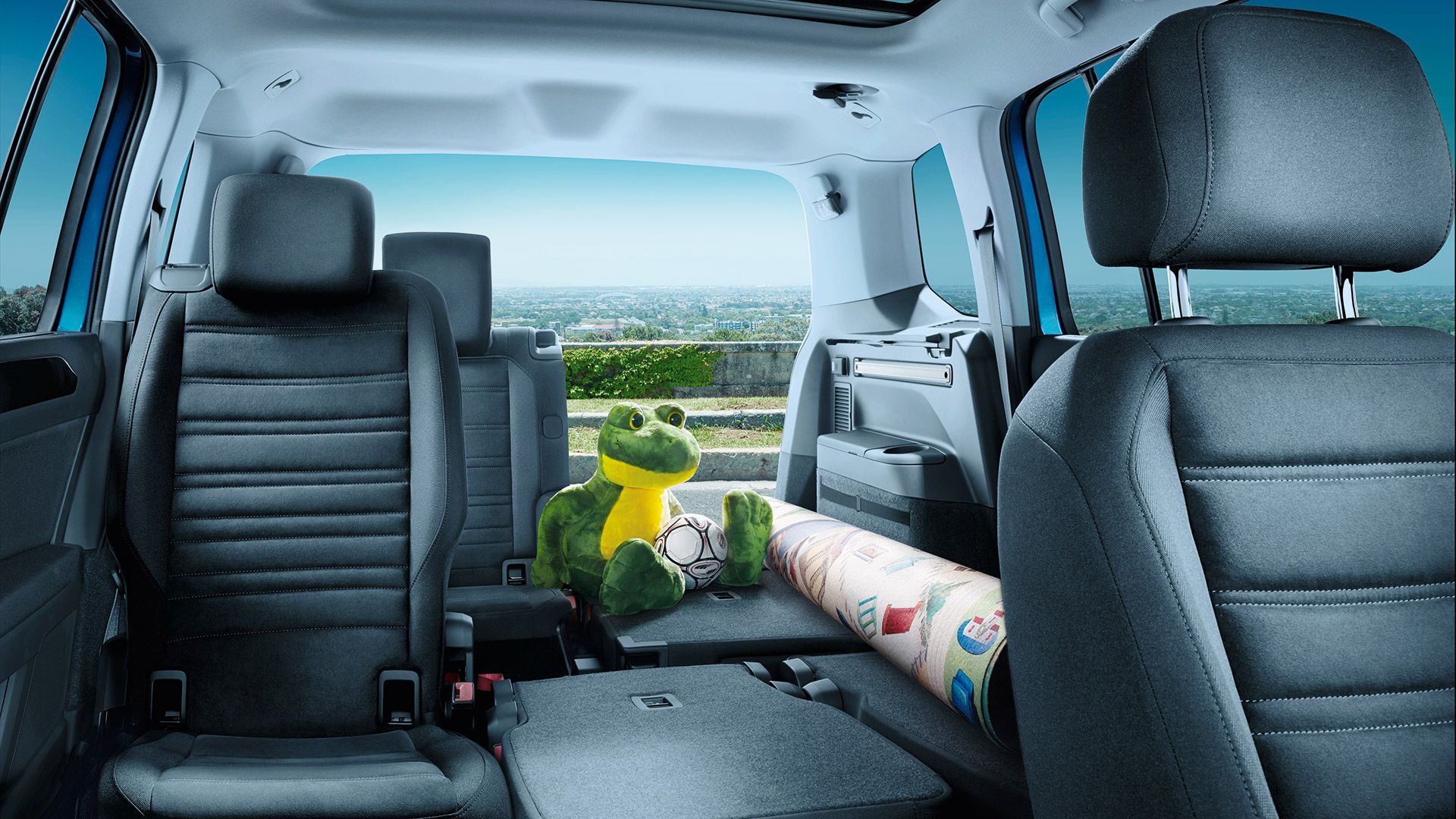 Umgeklappte Rücksitzbänke des VW Touran, ein eingerollter Teppich und ein Froschkuscheltier liegen auf der freien Fläche. 