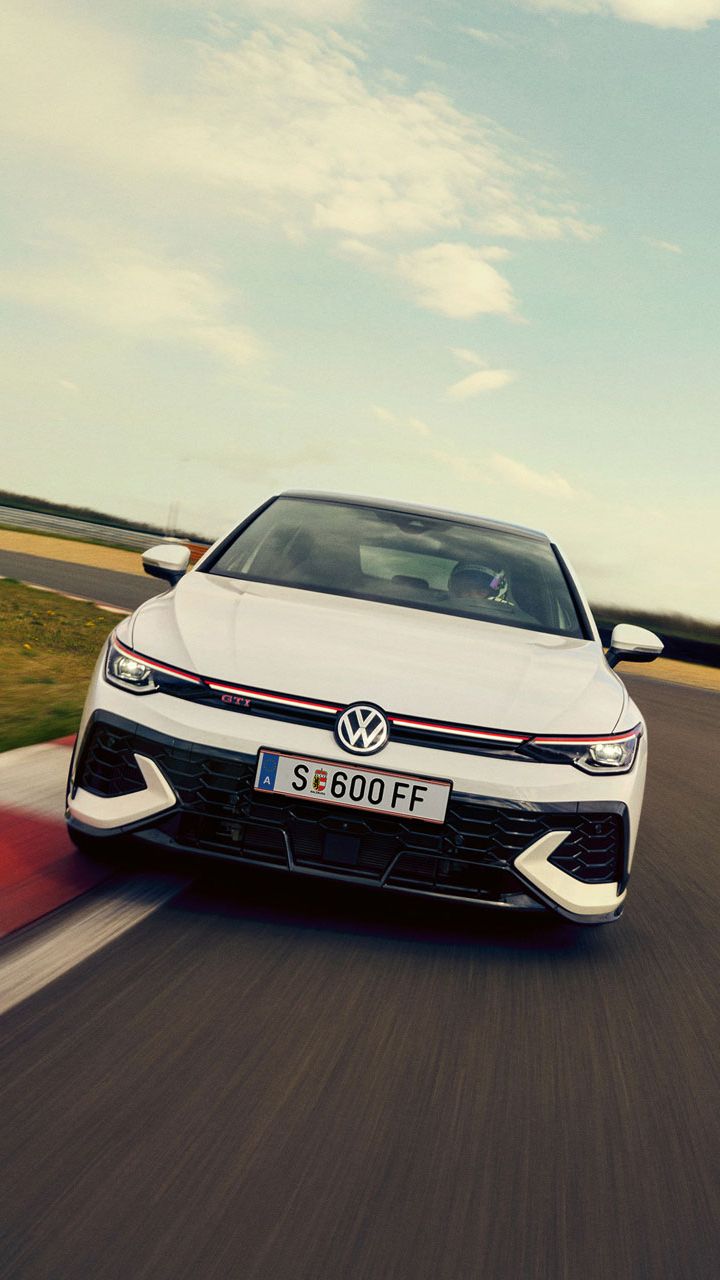 Frontansicht eines weißen VW Golf GTI Clubsport, der auf einer Rennstrecke in eine Kurve fährt.