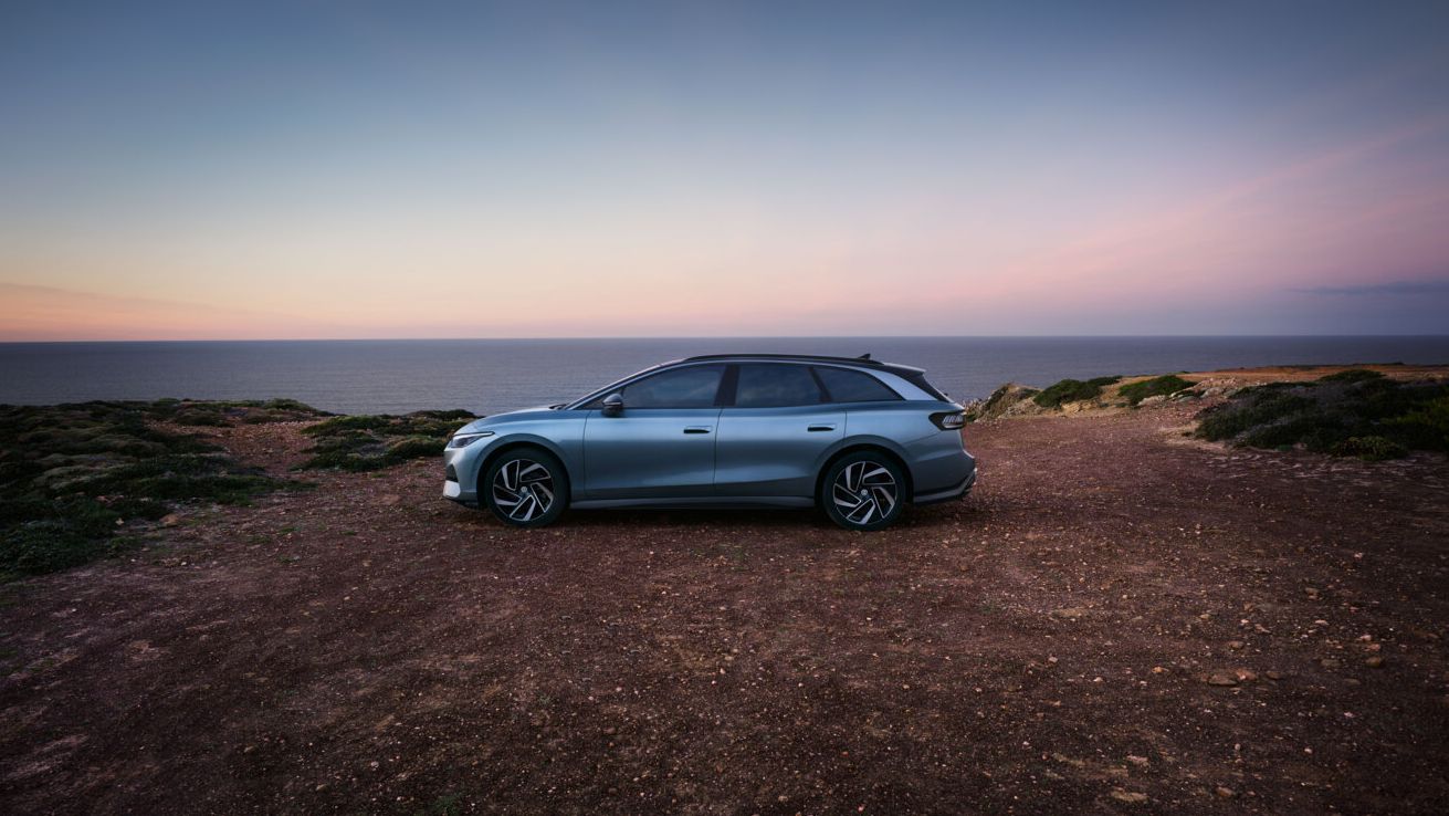 Ein blauer VW ID.7 Tourer steht oben auf einer Klippe im Sonnenuntergang, dahinter das Meer.