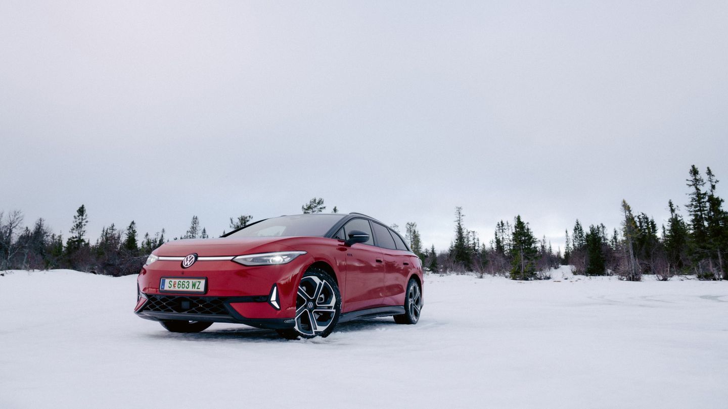 Ein roter ID.7 steht auf einer verschneiten Fläche, umgeben von vereinzelt stehenden Nadelbäumen. Die Umgebung wirkt kühl und winterlich. Der Himmel ist bewölkt und es herrscht eine ruhige Atmosphäre.