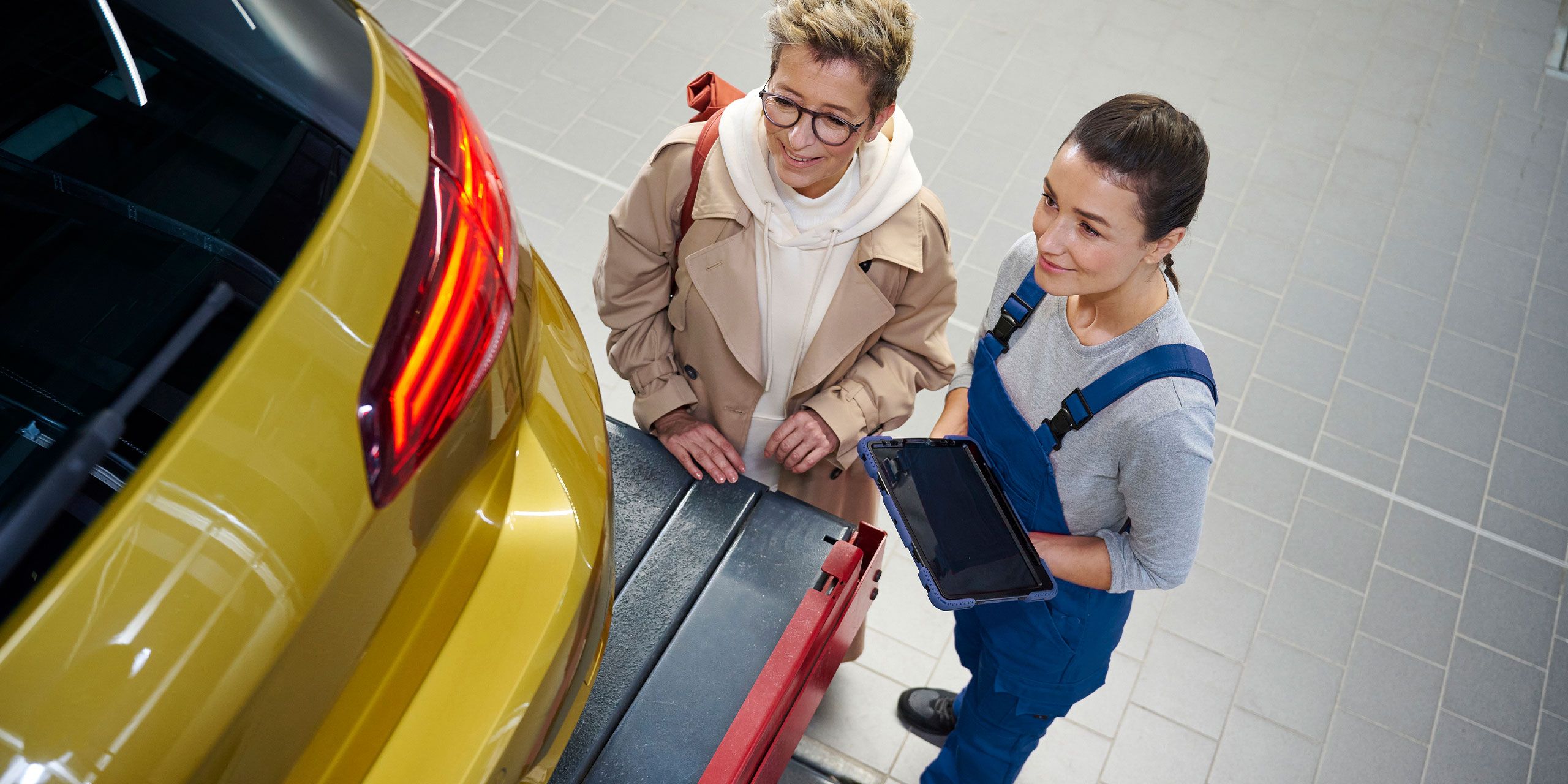 Zwei Personen stehen neben dem Kofferraum eines gelben VW Golf in einer Werkstatt.