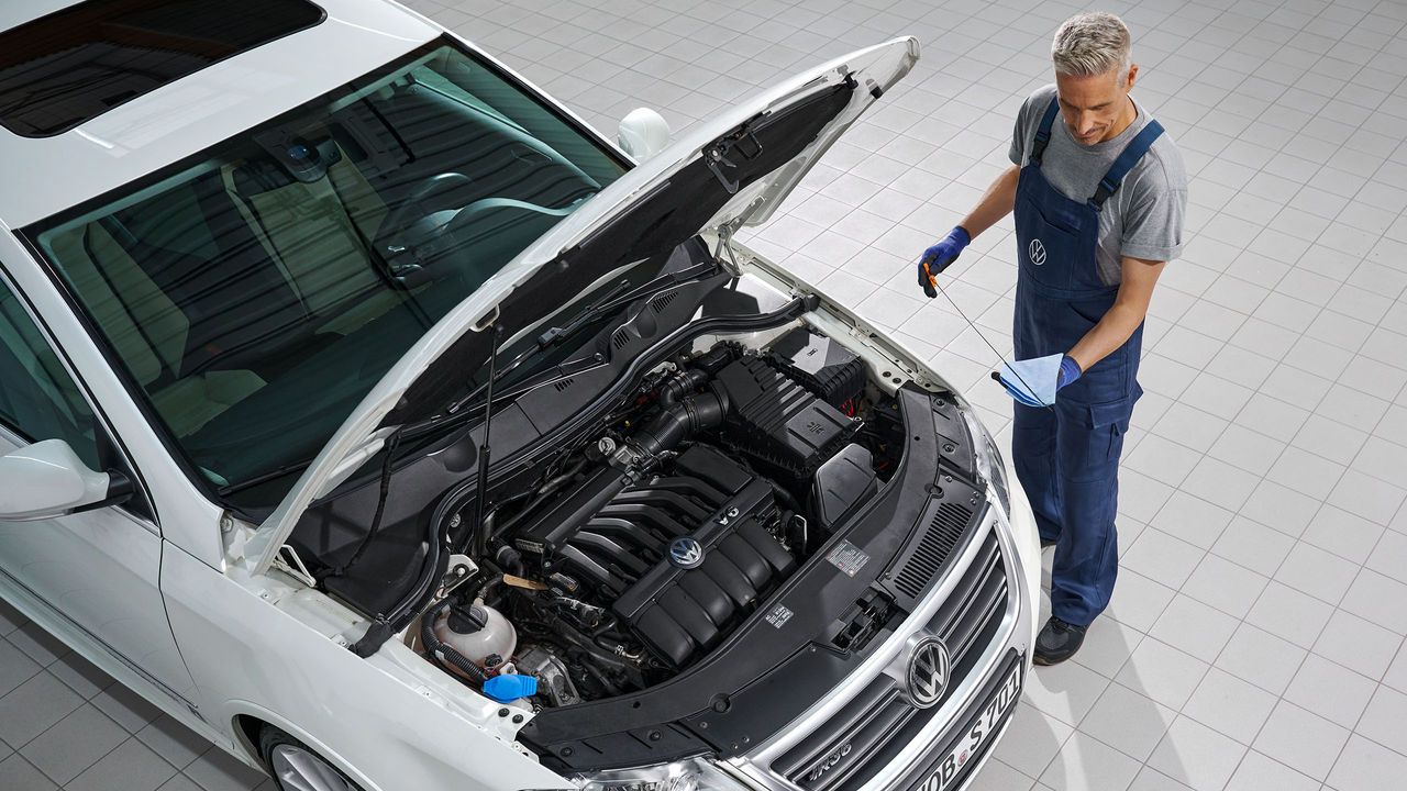 Ein Volkswagen Mechaniker wechselt Öl bei einem weißen Volkswagen Passat.